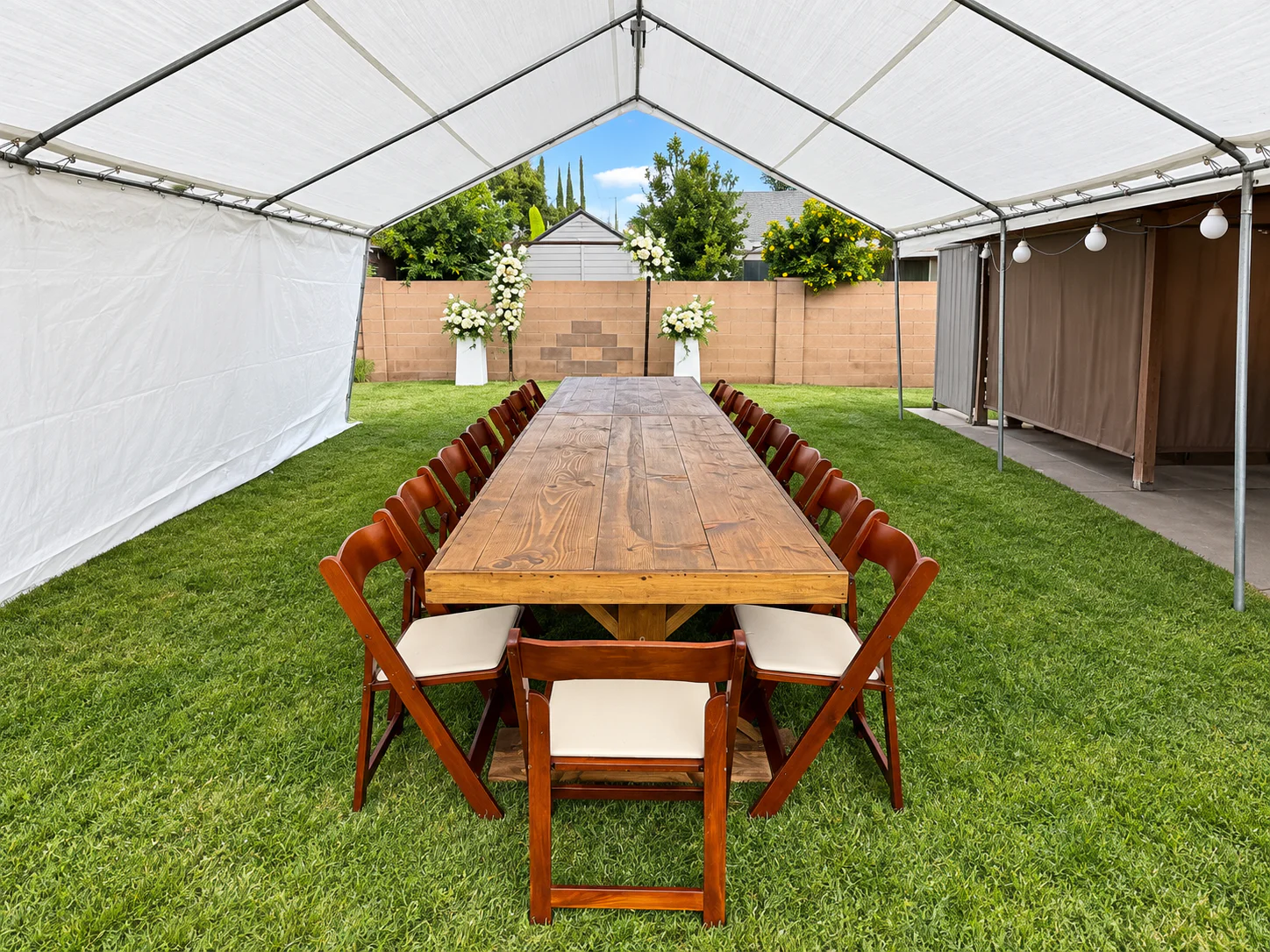 Long rustic table with brown folding chairs under a backyard canopy